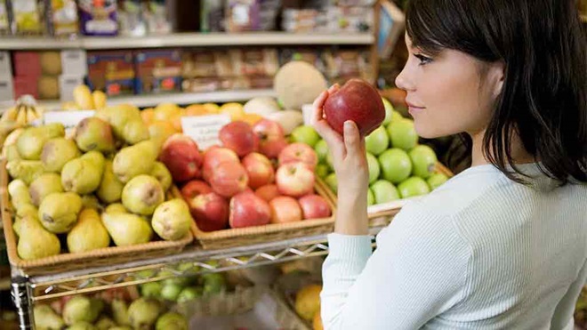 woman in supermarket picks up apple